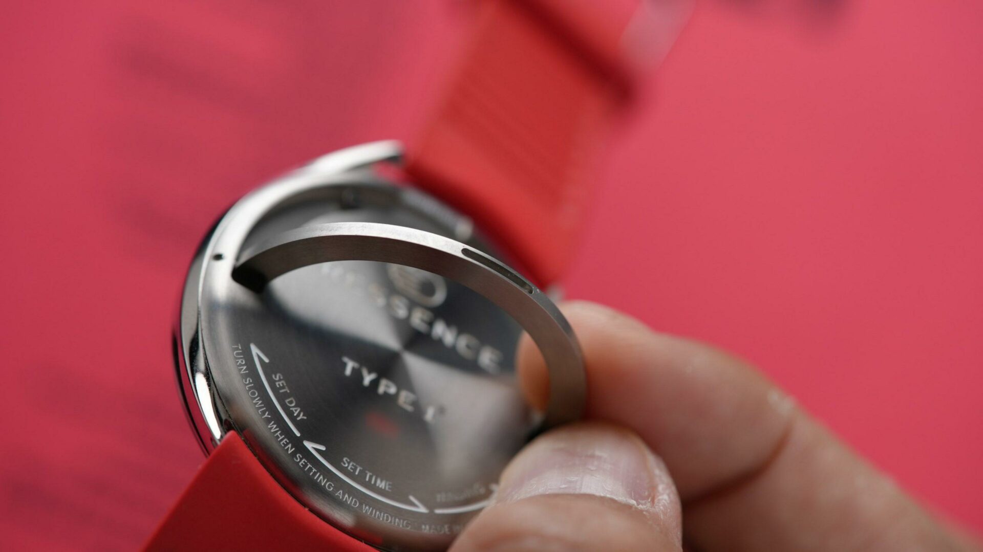 The back side of the Ressence Type 1 Slim Red being adjusted and held in hand closeup with red background.
