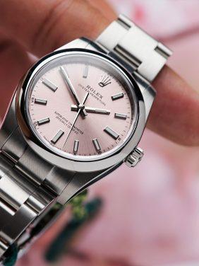 Rolex Oyster Perpetual 34 Pink Dial 2022 held in hand with pink flowers in background.