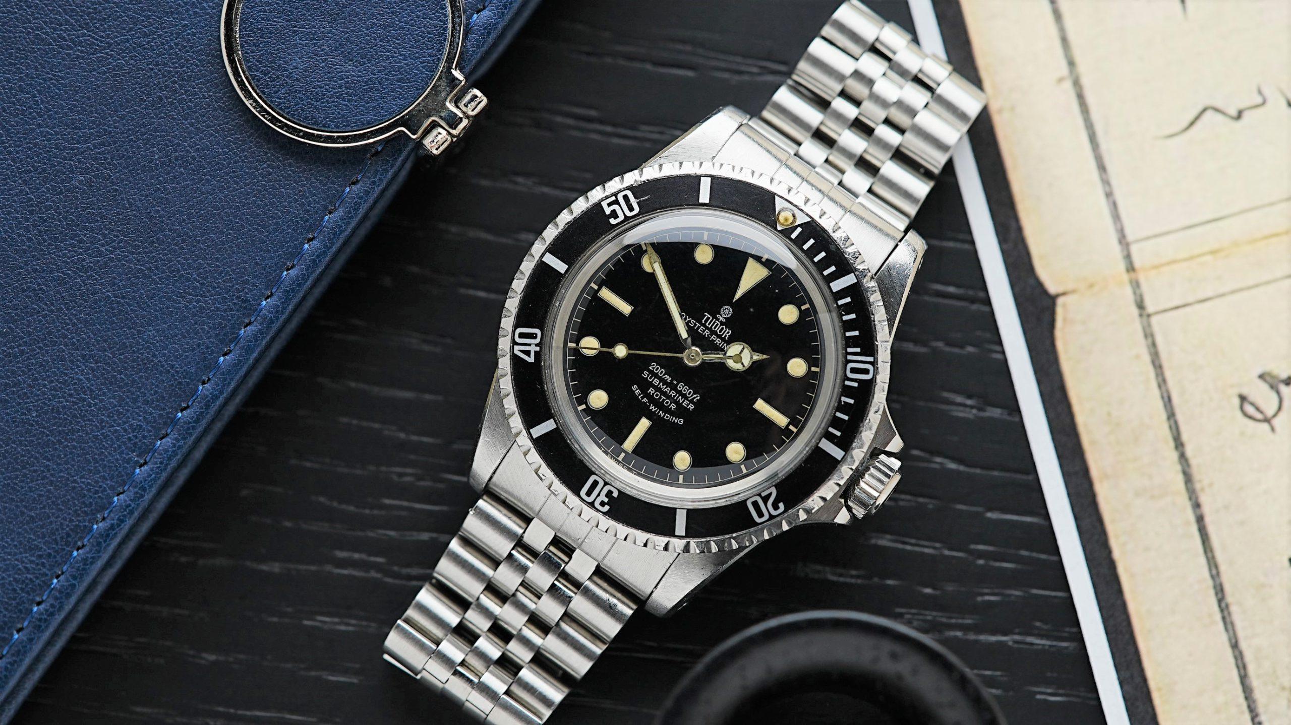 Tudor Submariner 7928 Gilt Patina featured under white light with blue notebook in background.