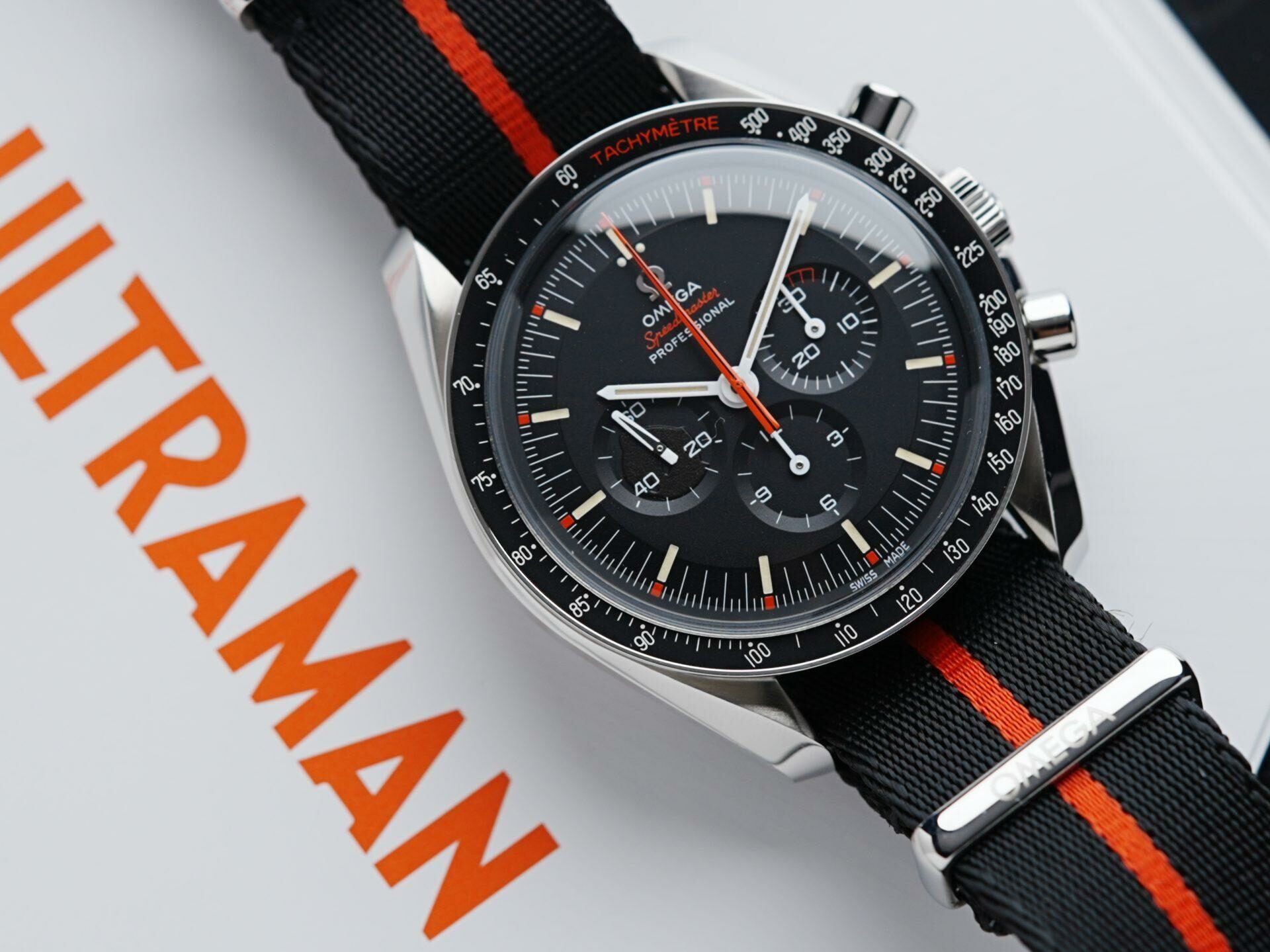Omega Speedy Tuesday Ultraman watch featured on white background with orange text reading 