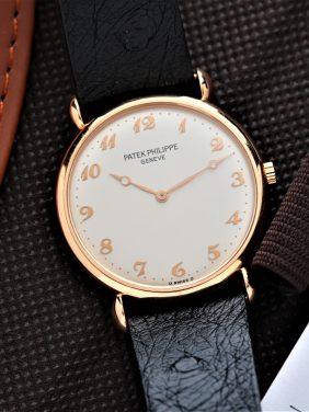 Patek Philippe Calatrava 32mm watch pictured beside leather book and paper udner white lighting..