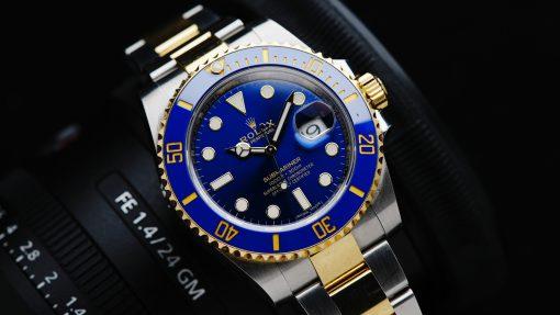 Rolex Submariner Blusey Two Tone Ceramic watch with camera in background.