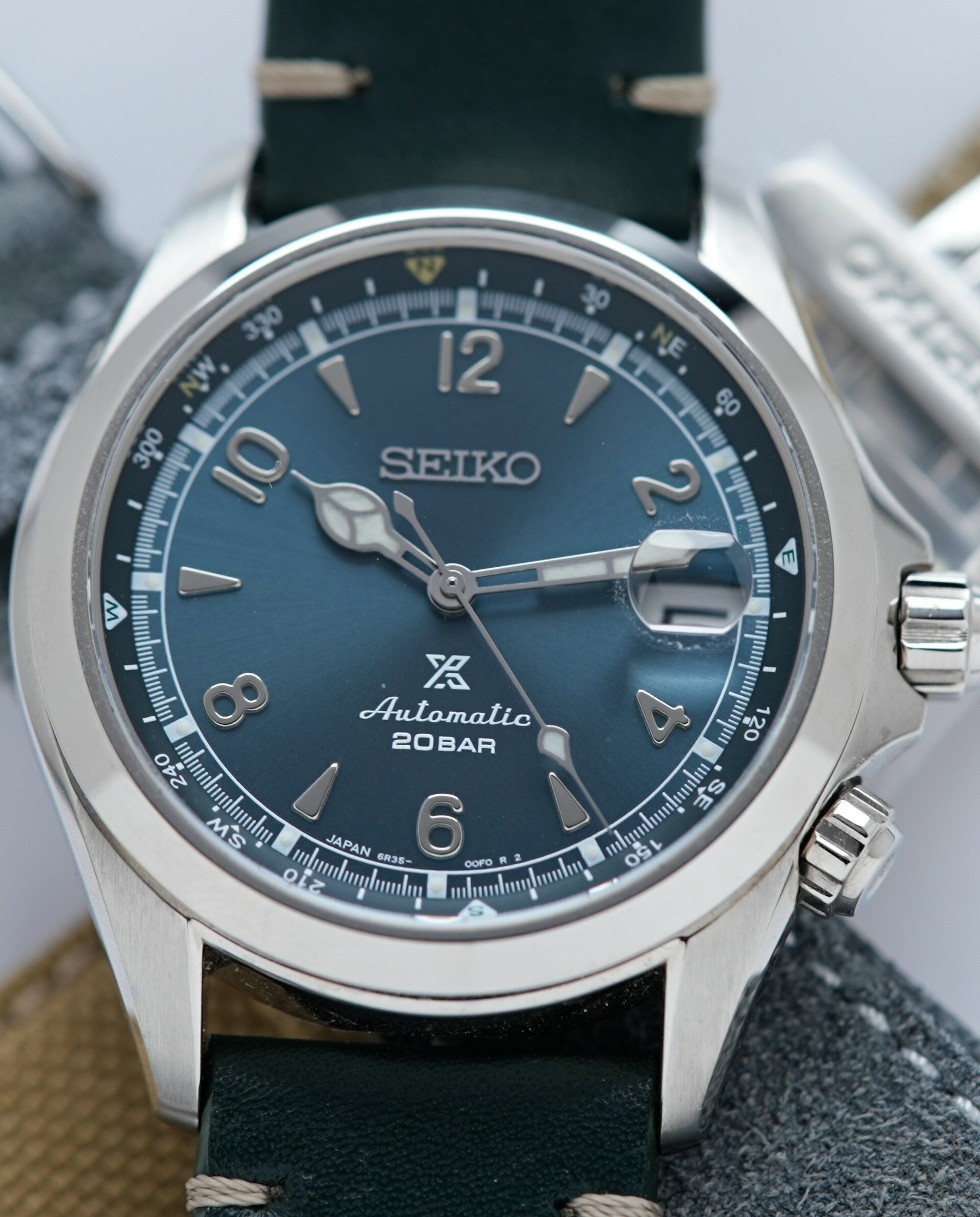 Seiko Alpinist Limited Edition Alpinist Mountain Glacier SPB199J1 watch on display along with two additional straps in the background.